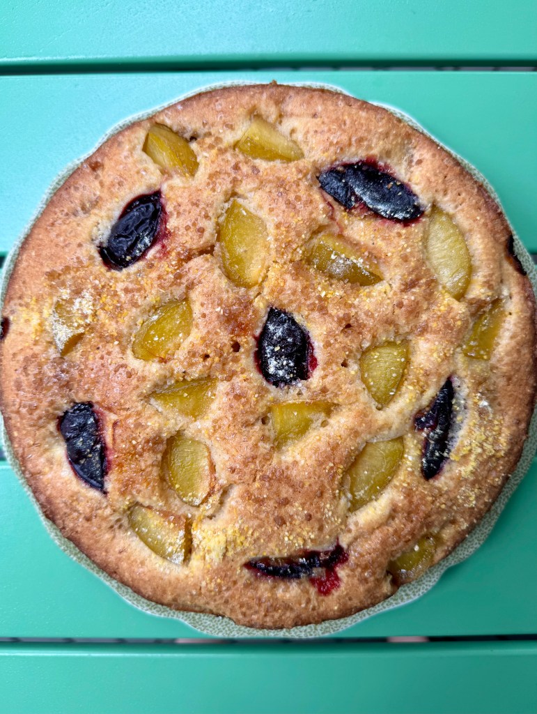 photo of a round cake with pieces of purple and green plum showing on the top