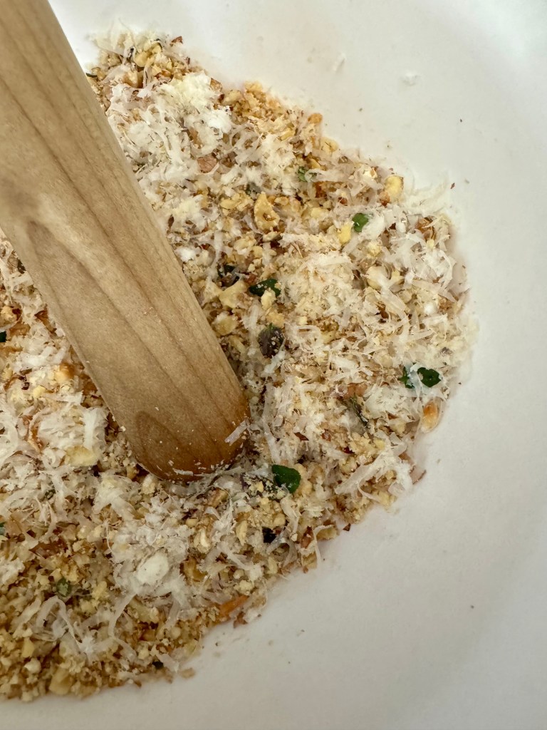 photo of walnuts, parmesan cheese, and other ingredients being crushed by a pestle