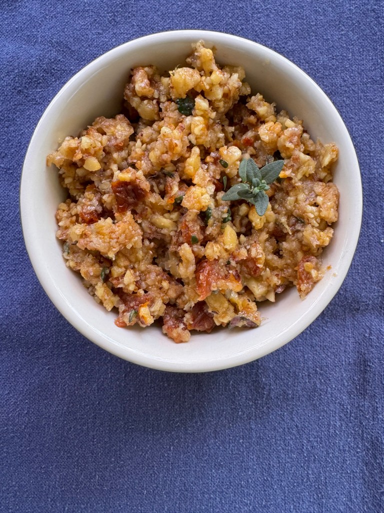 a small bowl of walnut and sun-dried tomato with a small sprig of thyme as garnish
